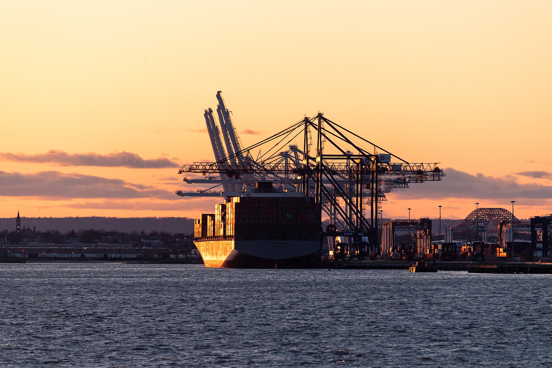 Container ship docked at the Port of New York and New Jersey at dusk, with gantry cranes loading colorful shipping containers